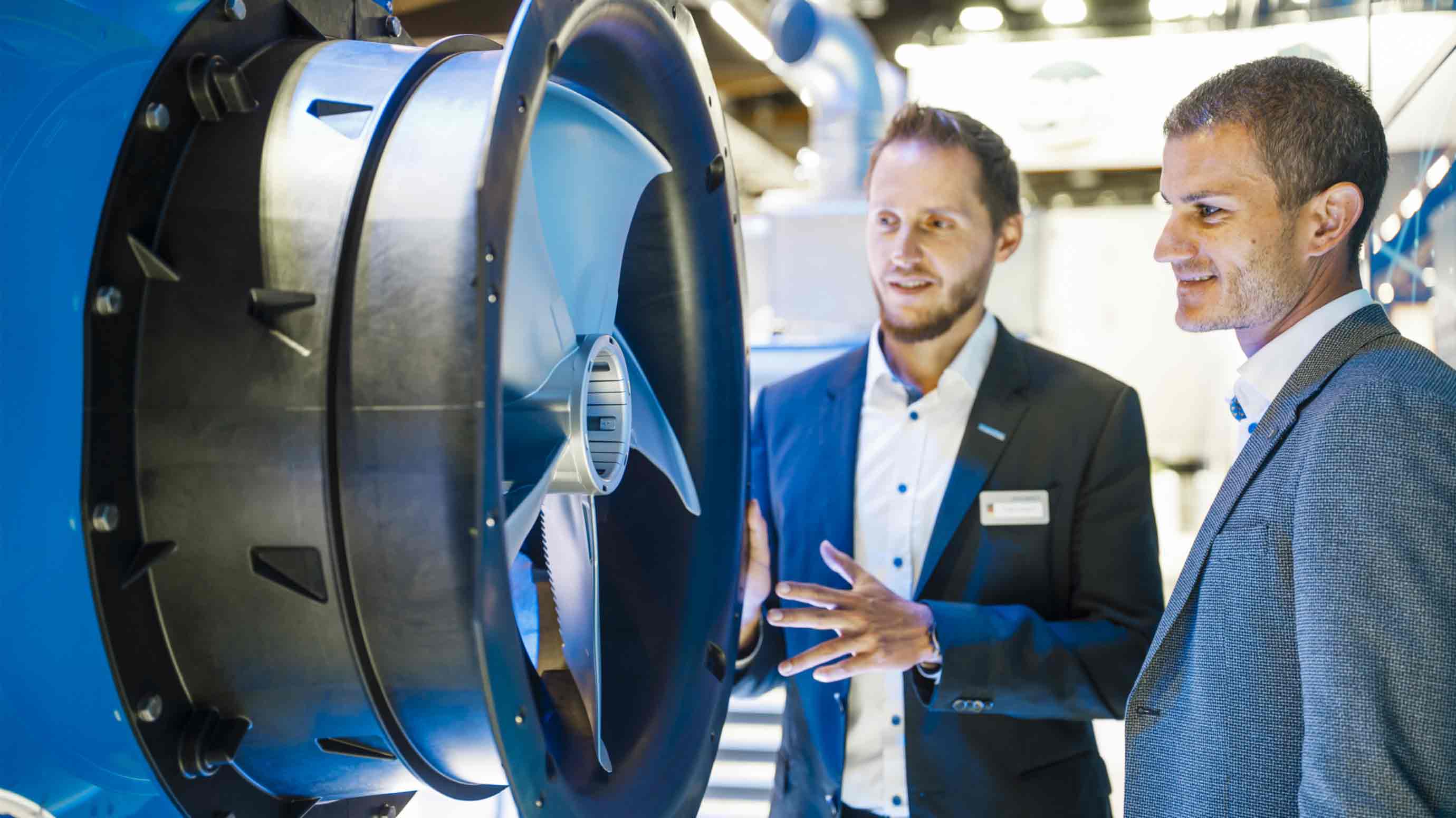 Two male trade fair participants stand in front of a turbine